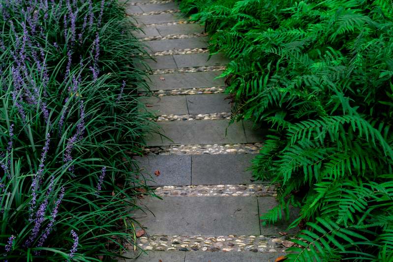 Hands laying interlocking concrete pavers along a garden edge with trowel and level visible